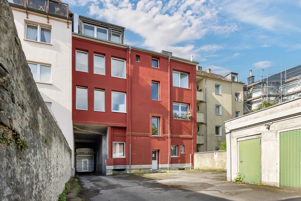 Mehrfamilienhaus mit roter Fassade, Garagen und gepflastertem Hof im Vordergrund.