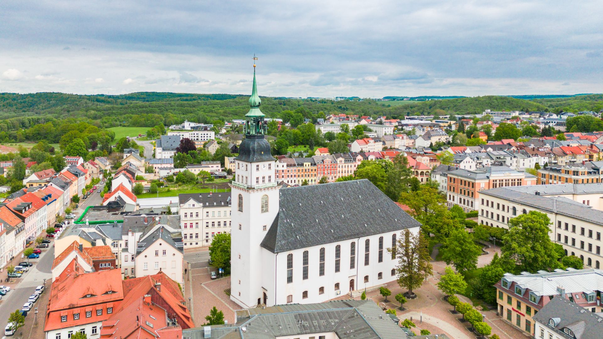 Luftaufnahme einer weißen Kirche mit Turm inmitten eines Wohnviertels mit vielen Häusern.