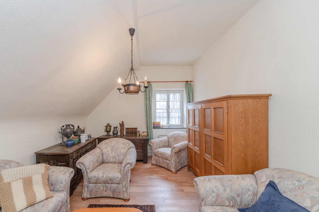 Gemütliches Wohnzimmer mit Sesseln, Holzschrank und kleinem Fenster mit Gardinen.