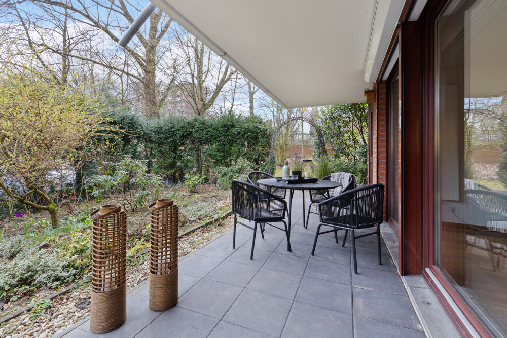 Überdachte Terrasse mit vier Stühlen, Tisch und zwei Laternen, Blick auf Garten.