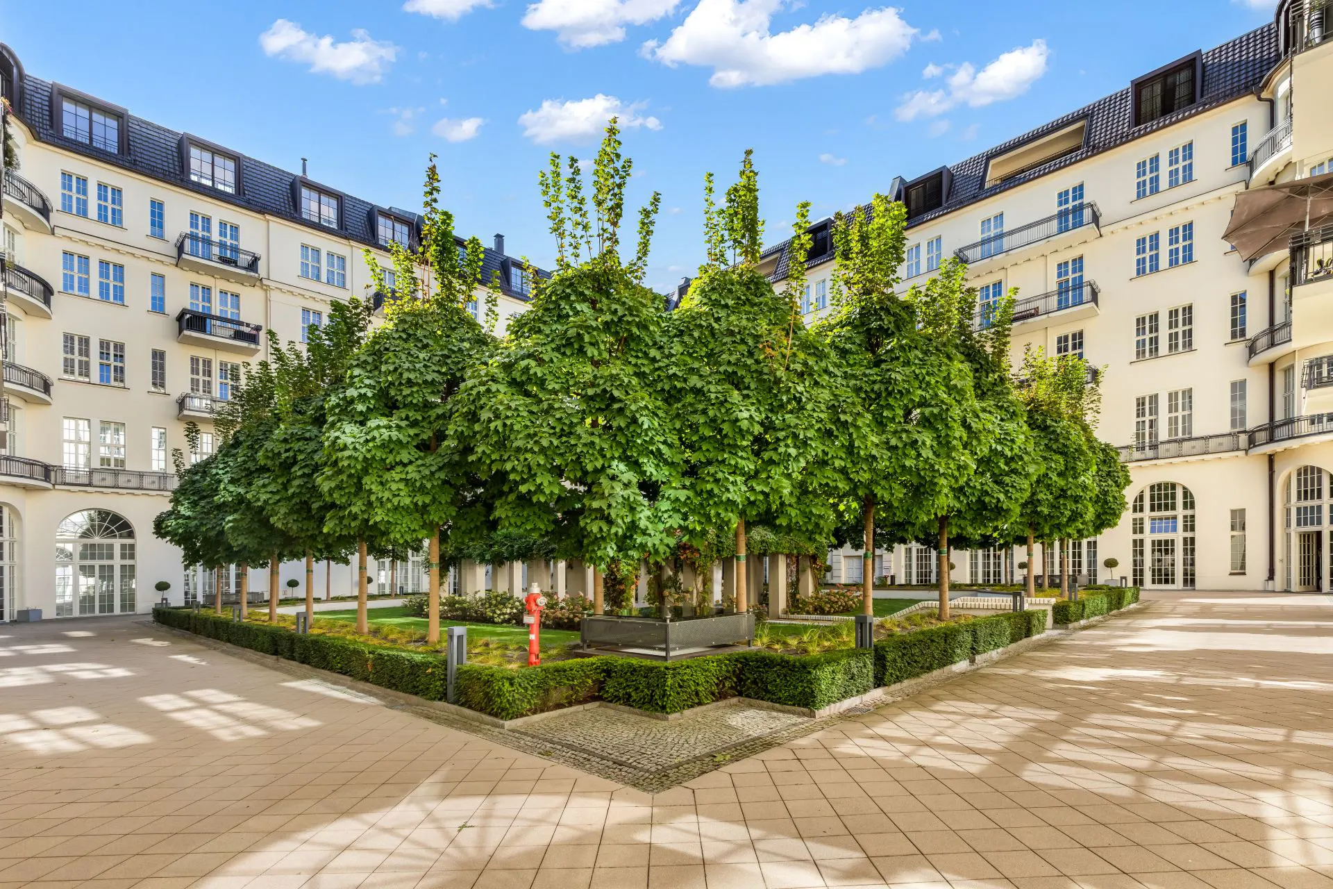 Innenhof mit Bäumen, gepflegtem Grün und mehrstöckigen Wohngebäuden im Hintergrund.