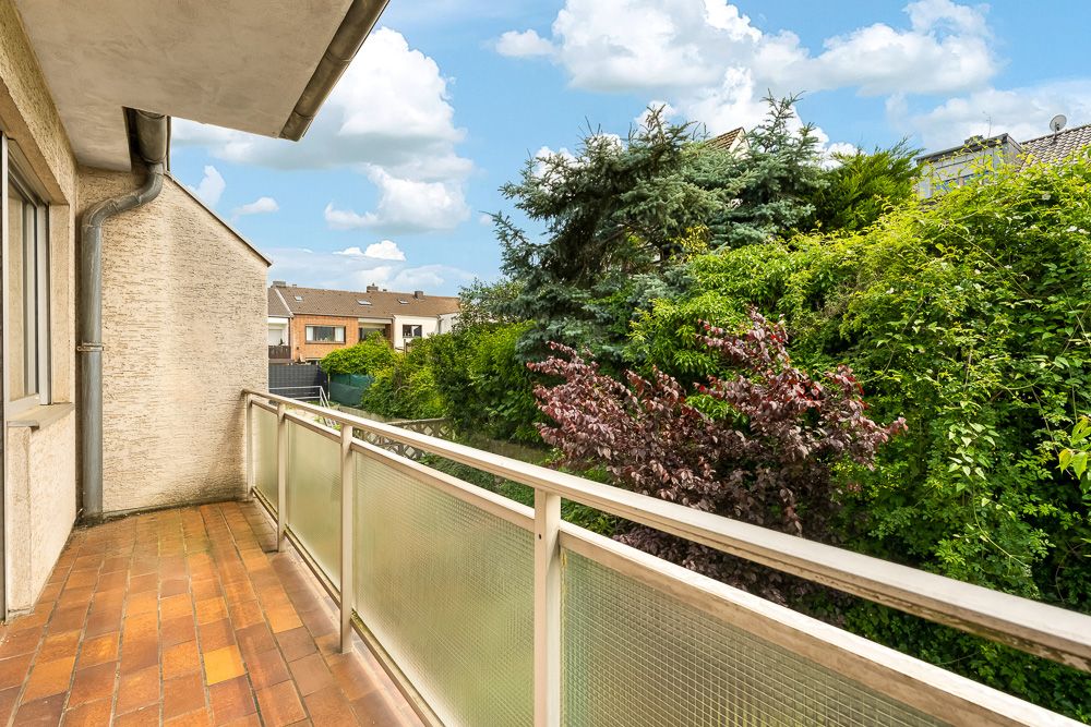 Balkon mit Glasgeländer und Blick auf dichte grüne Büsche und Bäume im Garten.