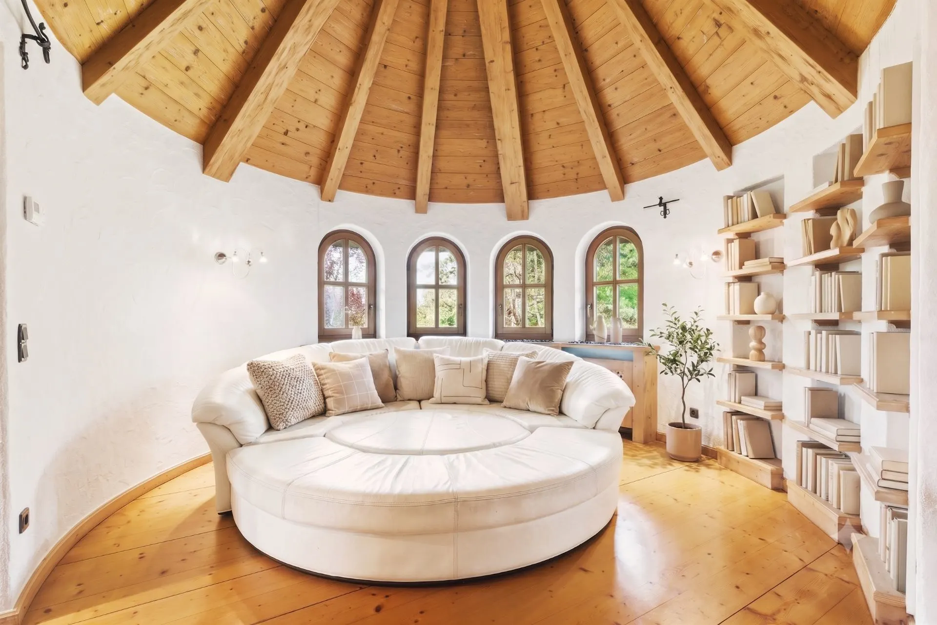 Helles Wohnzimmer mit rundem Sofa, Holzboden, Bücherregal und gewölbter Holzdecke.