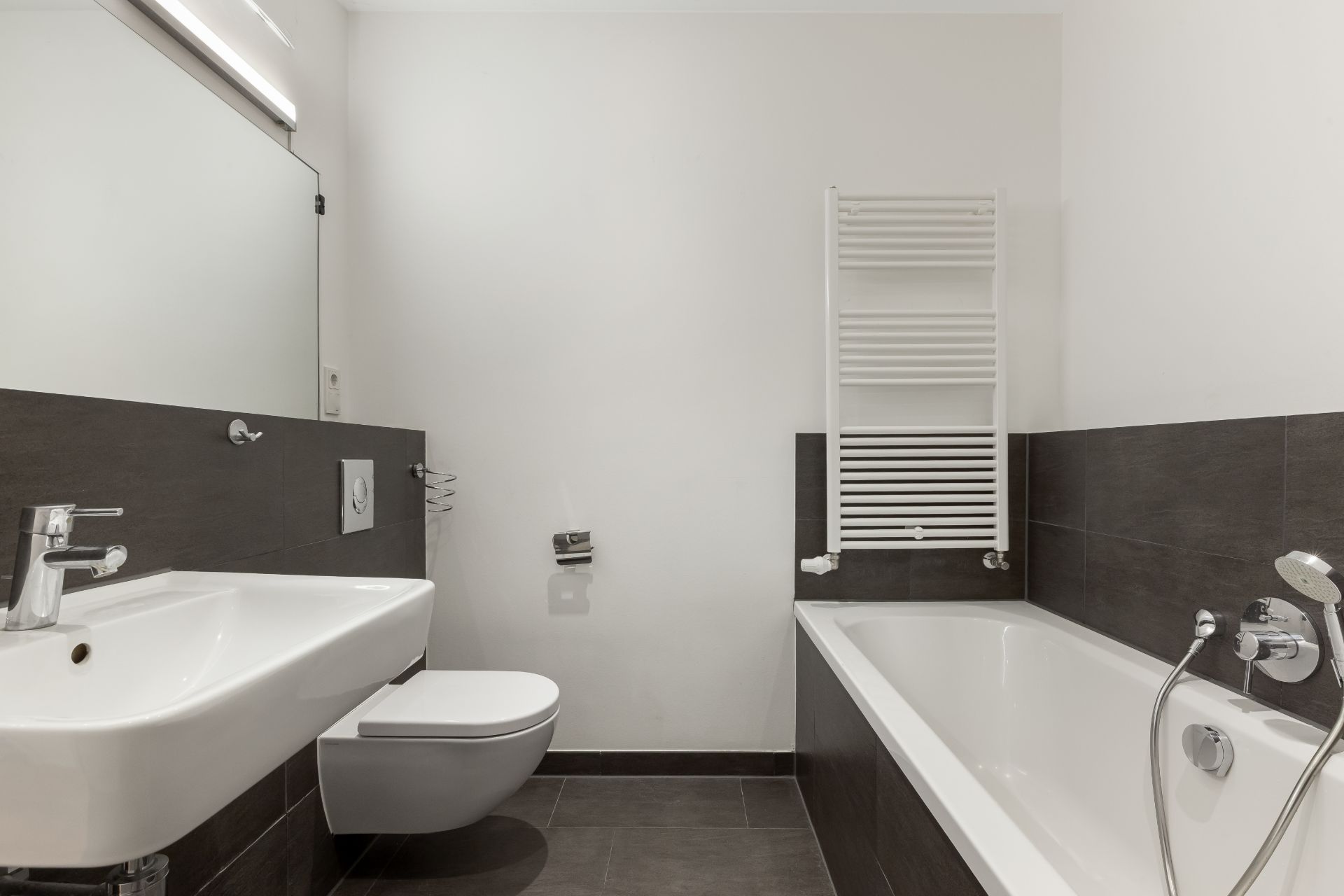 Modernes Badezimmer mit Waschbecken, Wandtoilette, Badewanne und Handtuchheizkörper.
