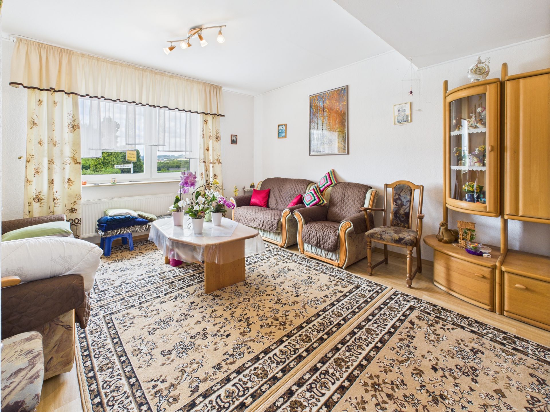 Wohnzimmer mit Teppich, Sofa, Sessel, Holzmöbeln und einem Fenster mit Vorhängen.
