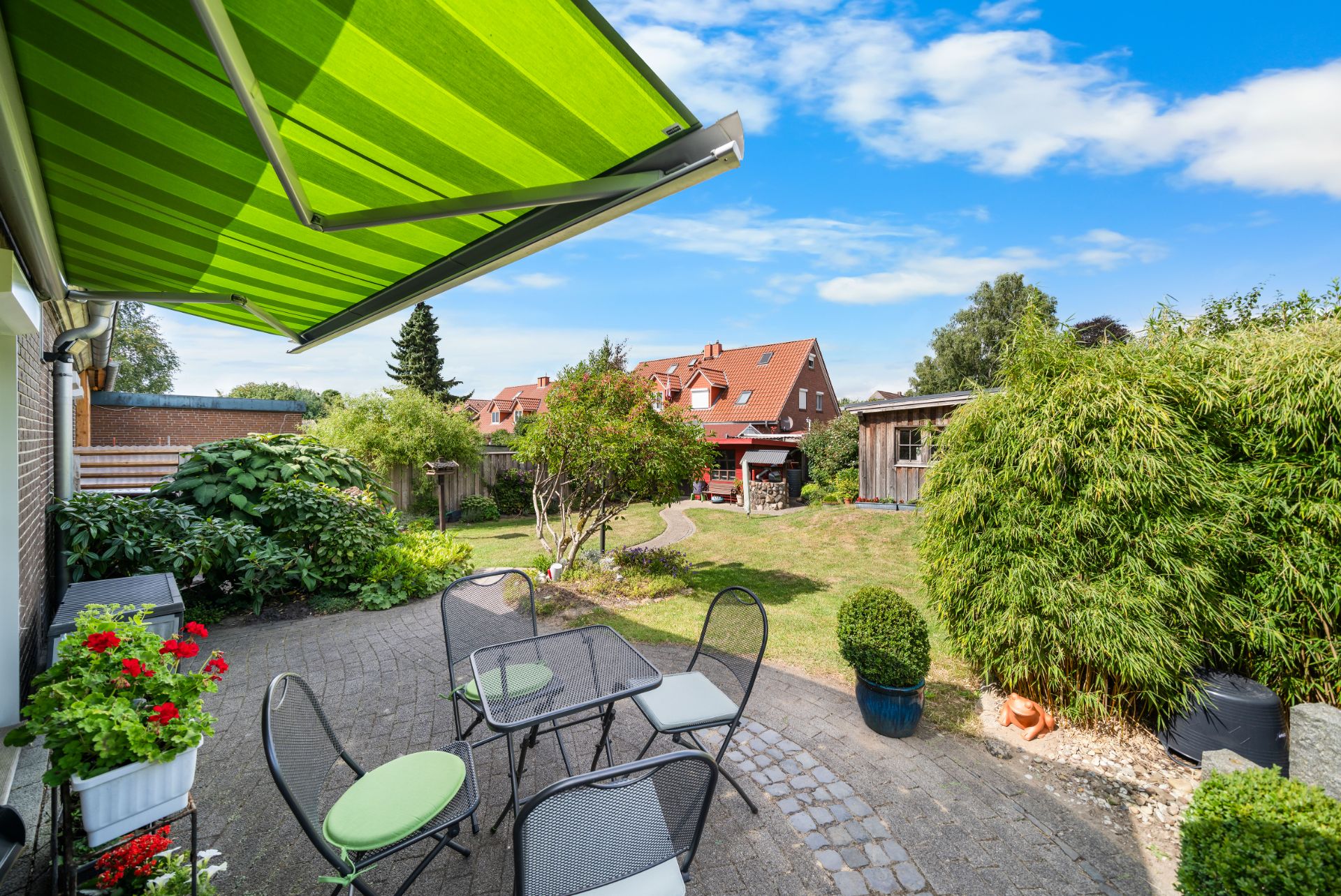 Terrasse mit grünem Sonnenschutz, Gartentisch und Stühlen, Blick in gepflegten Garten.