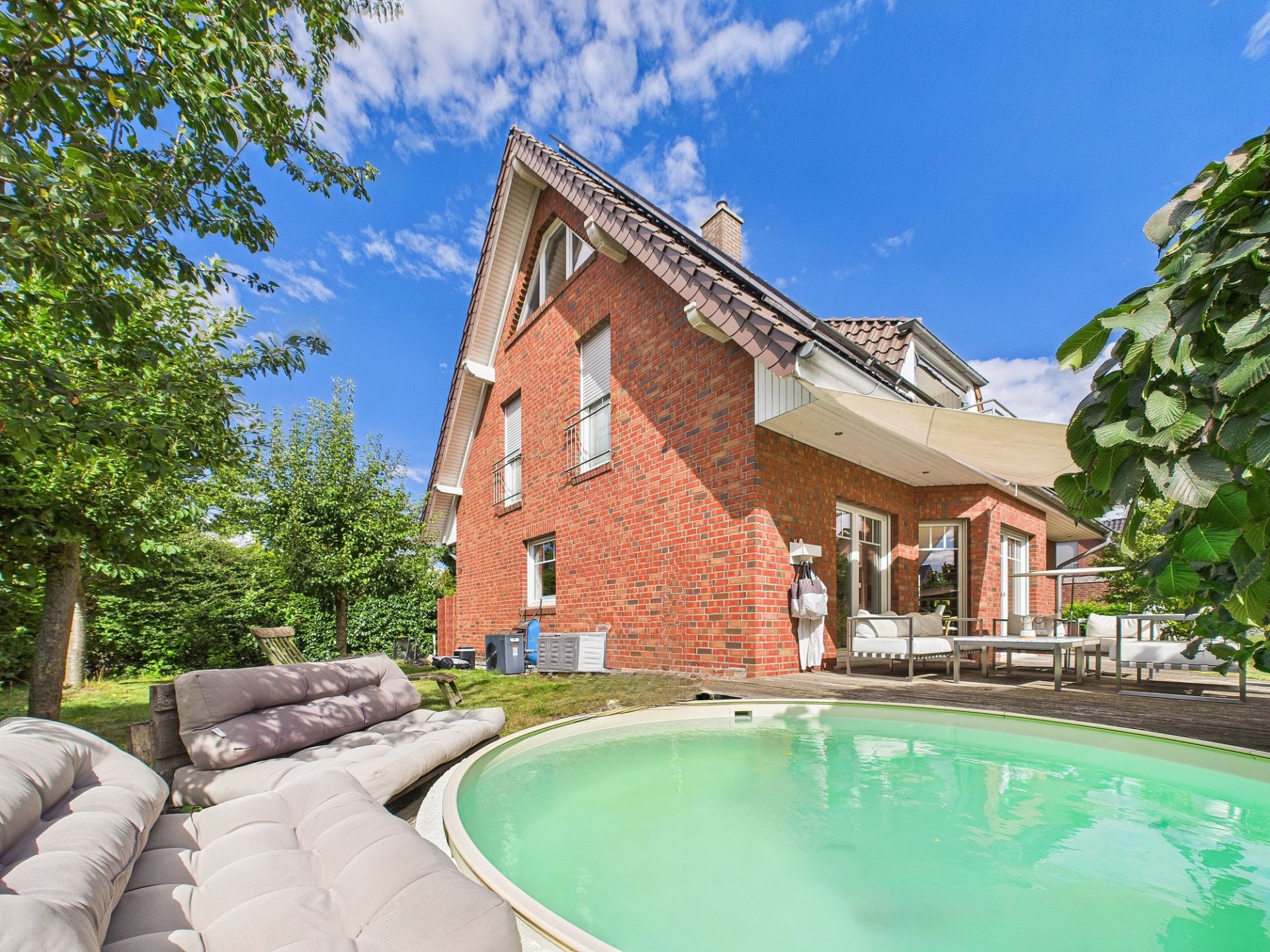 Backsteinwohnhaus mit Garten, Pool und Terrasse, umgeben von Bäumen und Gartenmöbeln.