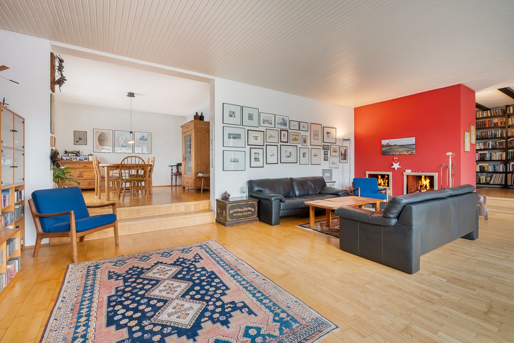 Wohnzimmer mit schwarzen Sofas, Kamin, roter Wand, Teppich und Essbereich auf erhöhter Ebene.