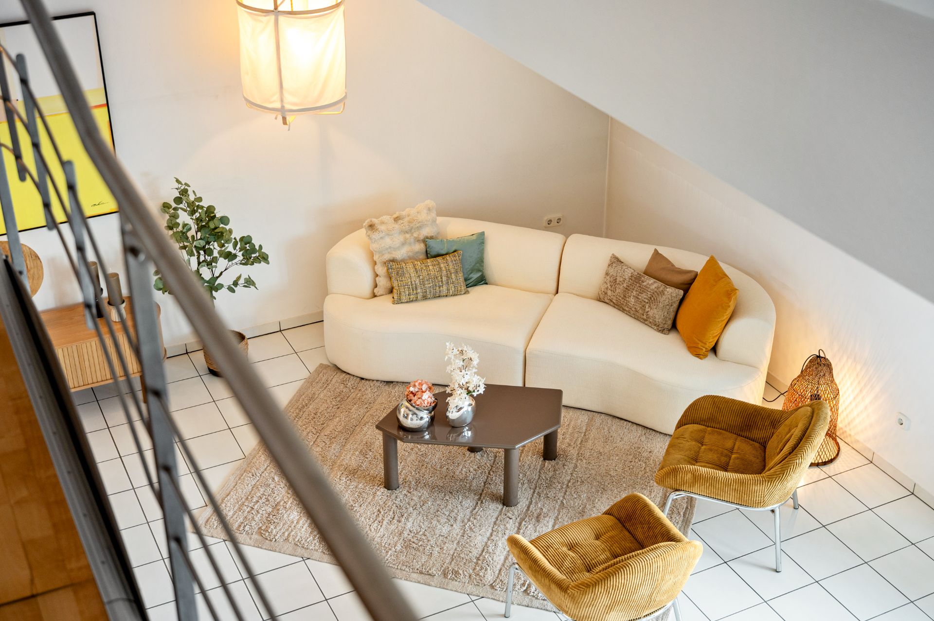 Wohnzimmer mit weißem Sofa, zwei gelben Sesseln, Couchtisch und Teppich auf weißem Fliesenboden.
