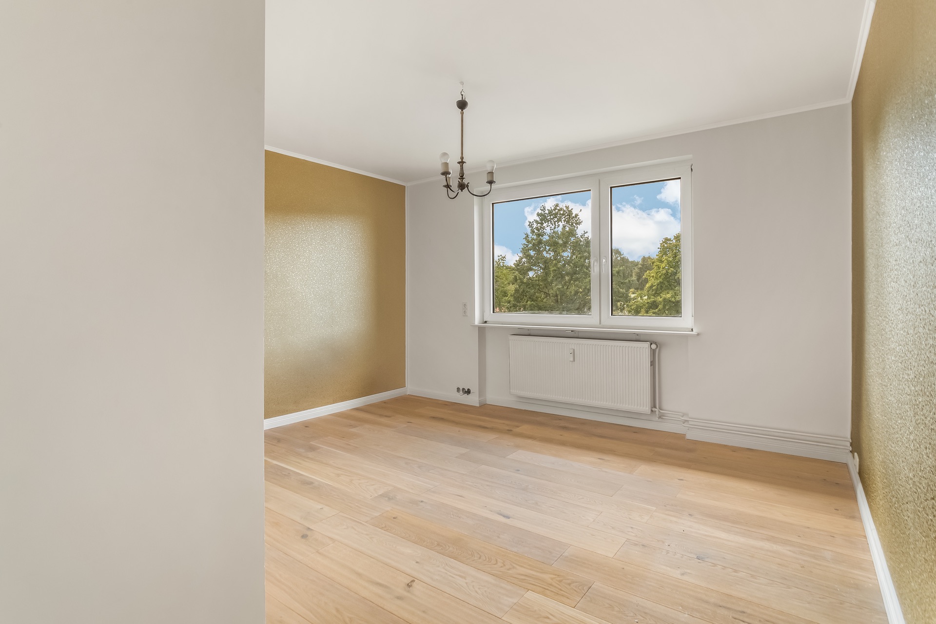Leerer Raum mit Holzfußboden, zwei Fenstern und einer kleinen Deckenlampe.