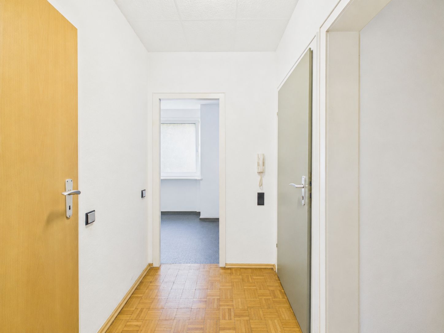 Heller Flur mit Parkettboden und mehreren Türen, Blick in ein angrenzendes Zimmer mit Fenster.