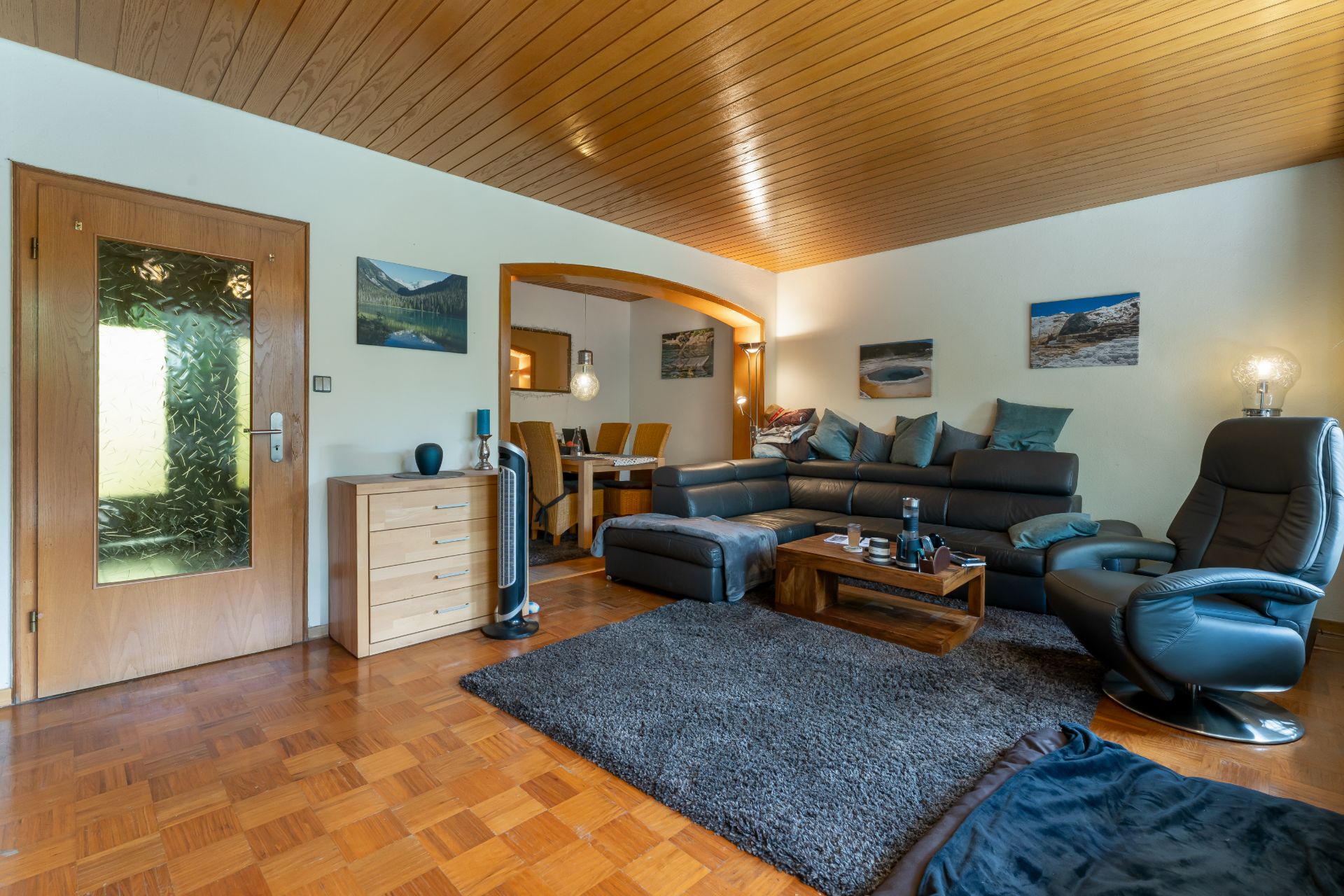 Modernes Wohnzimmer mit Ecksofa, Sessel, Teppich und Essbereich im Hintergrund.