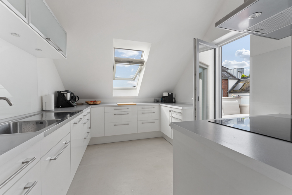 Moderne, helle Küche mit weißen Einbauten und Zugang zur Terrasse.