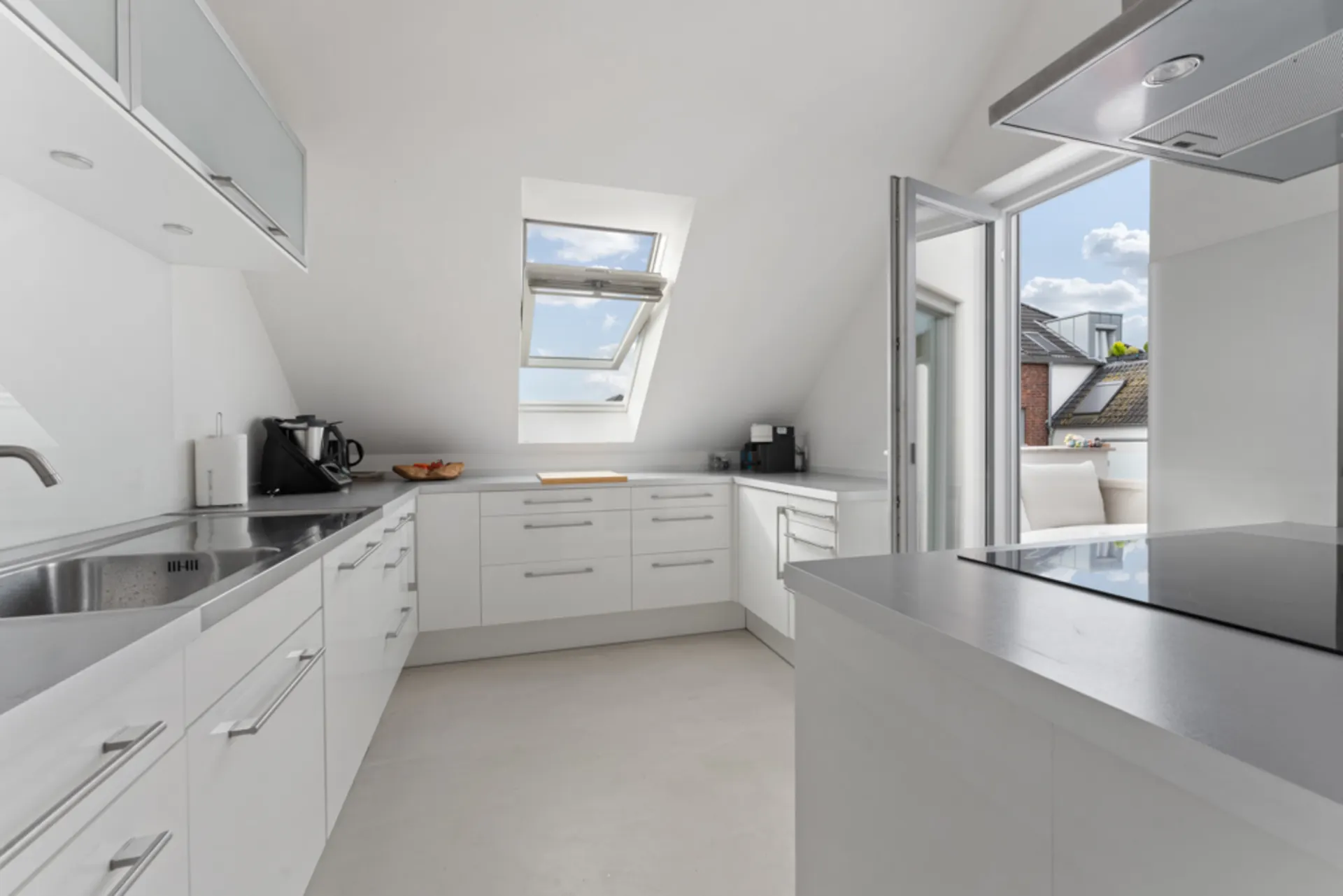 Moderne, helle Küche mit weißen Einbauten und Zugang zur Terrasse.