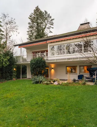 Zweistöckiges Wohnhaus mit großem Garten, Terrasse und umliegenden Bäumen.