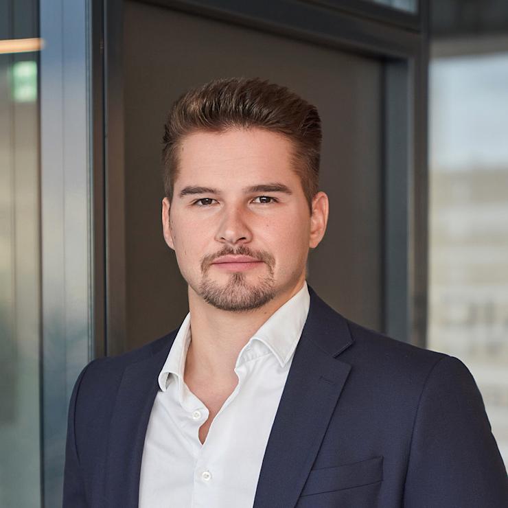 Ein Mann im Anzug steht vor einer Glaswand in einem modernen Innenraum.