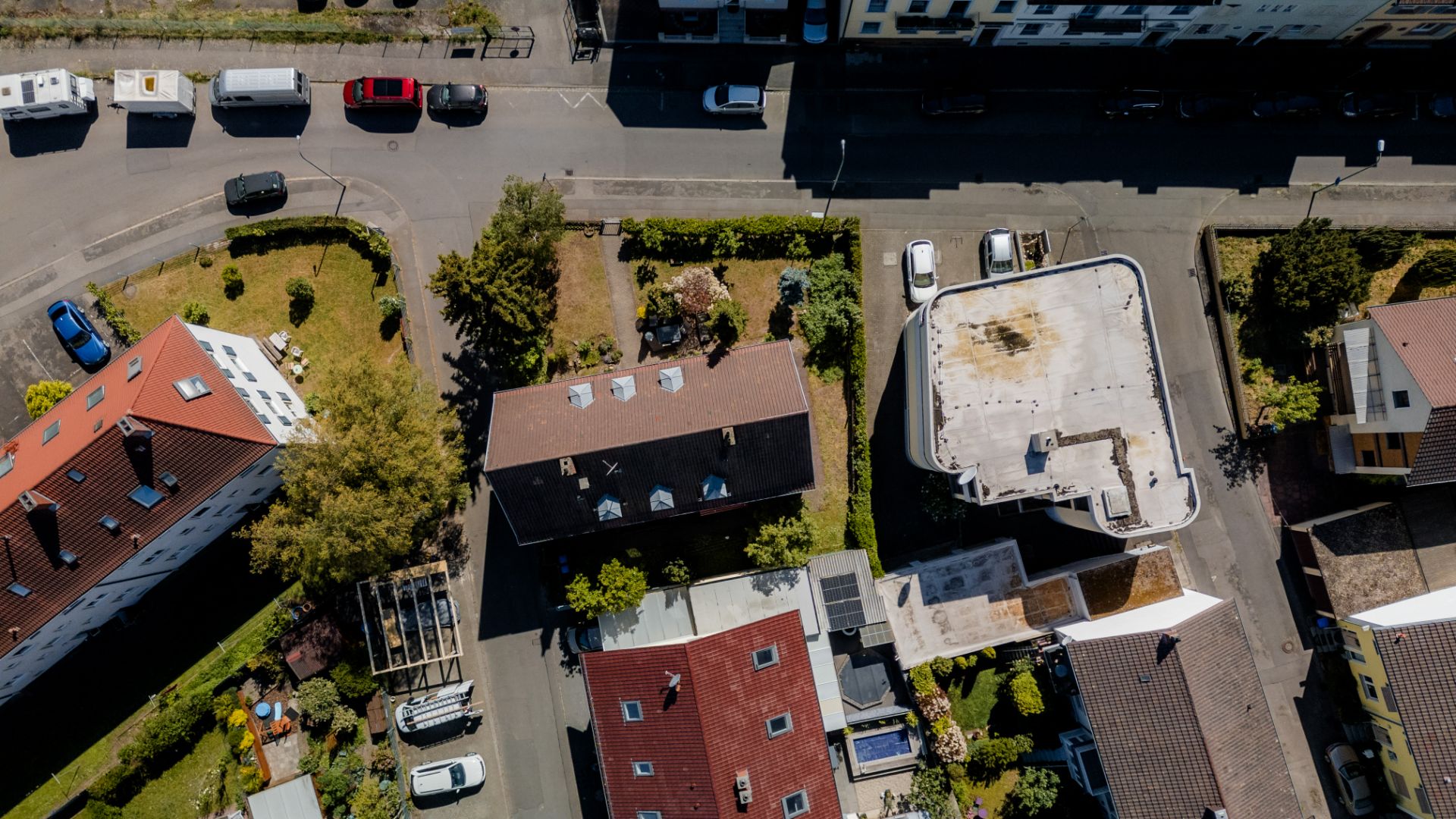 Luftaufnahme von Wohngebäuden mit Gärten, Straßen und parkenden Autos.
