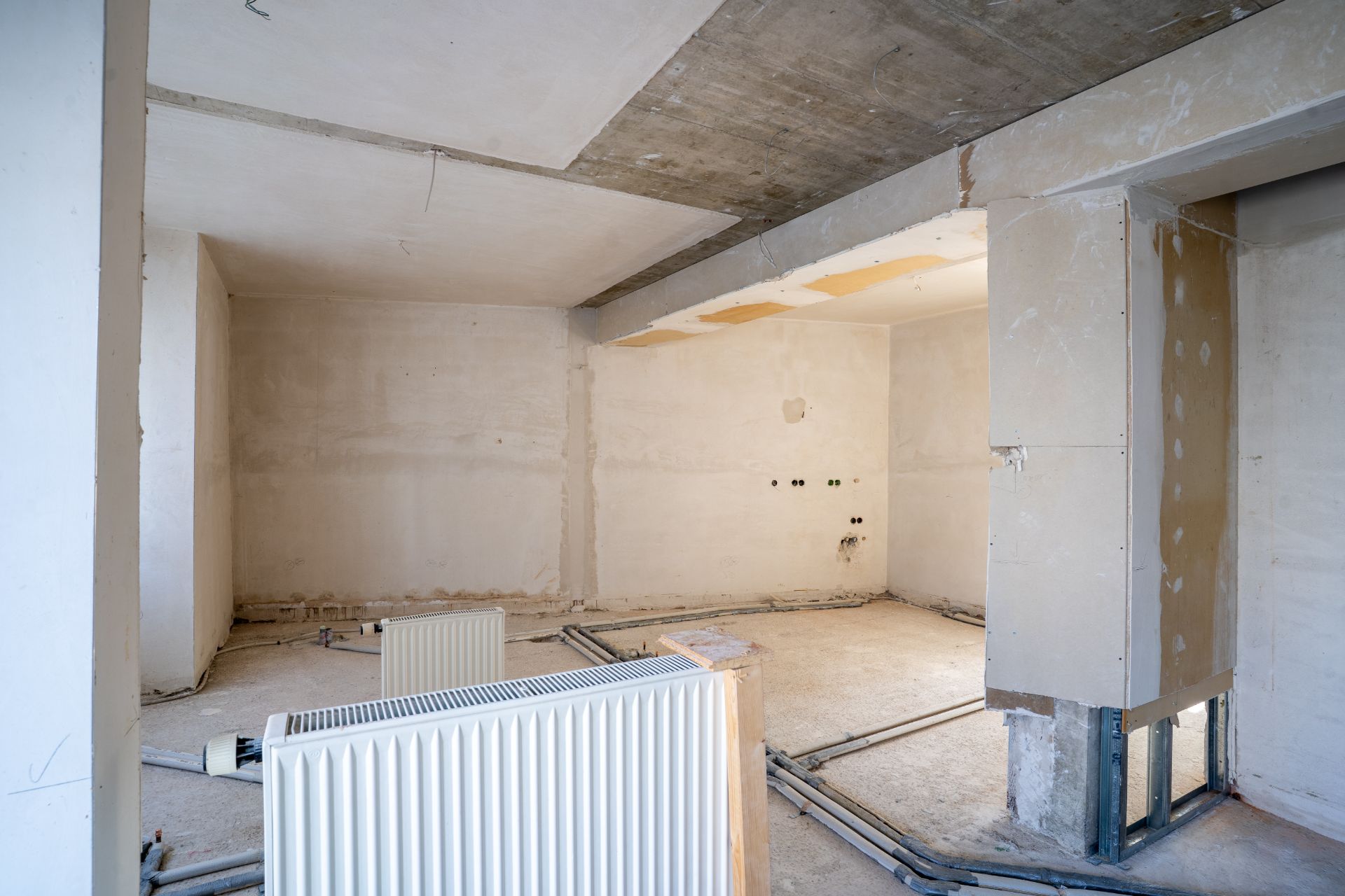 Rohbau eines Zimmers mit sichtbaren Heizkörpern und offenen Leitungen am Boden.