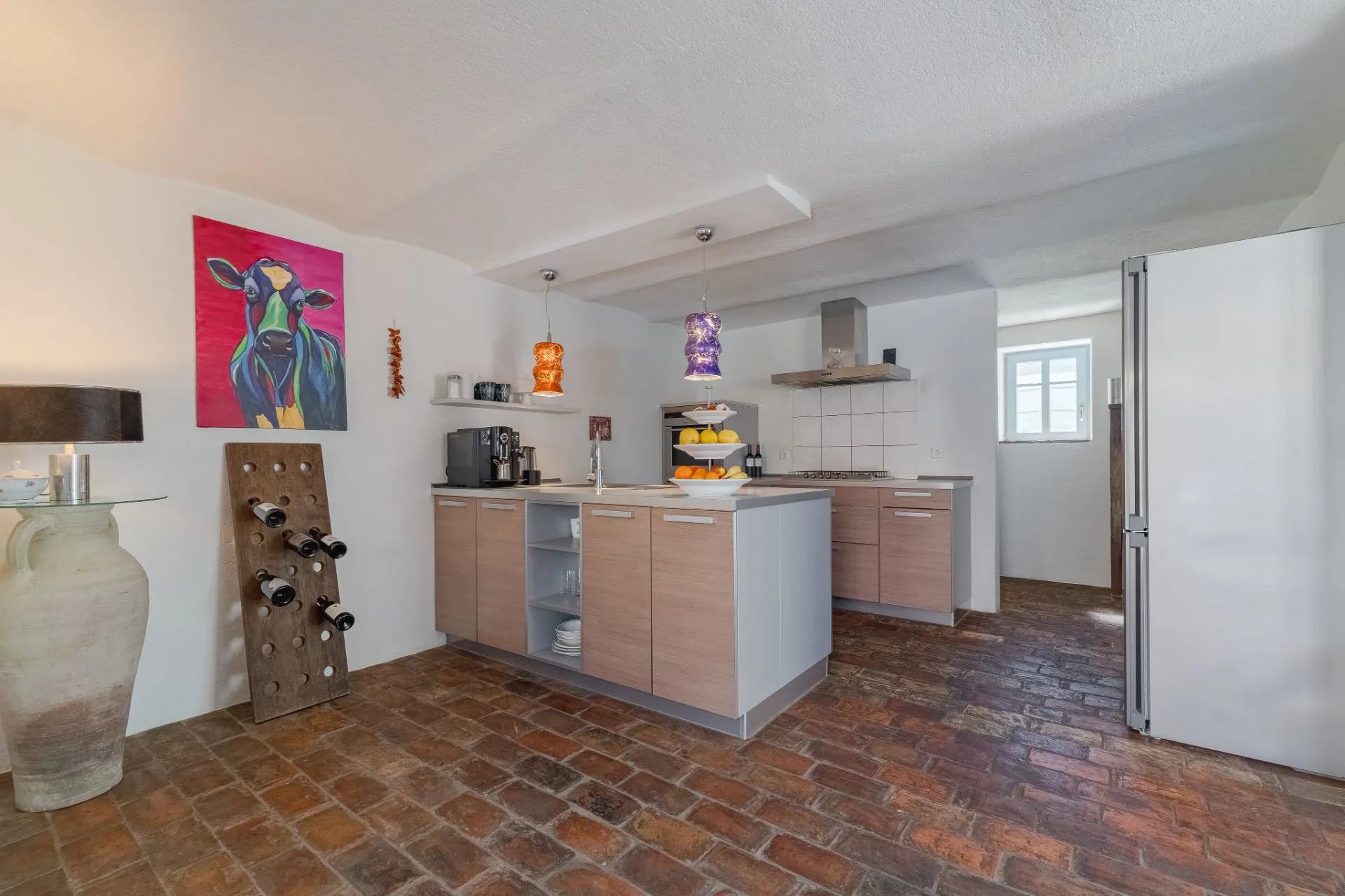 Helle Küche mit gemustertem Fliesenboden, Holzmöbeln und bunter Kuh-Malerei an der Wand.