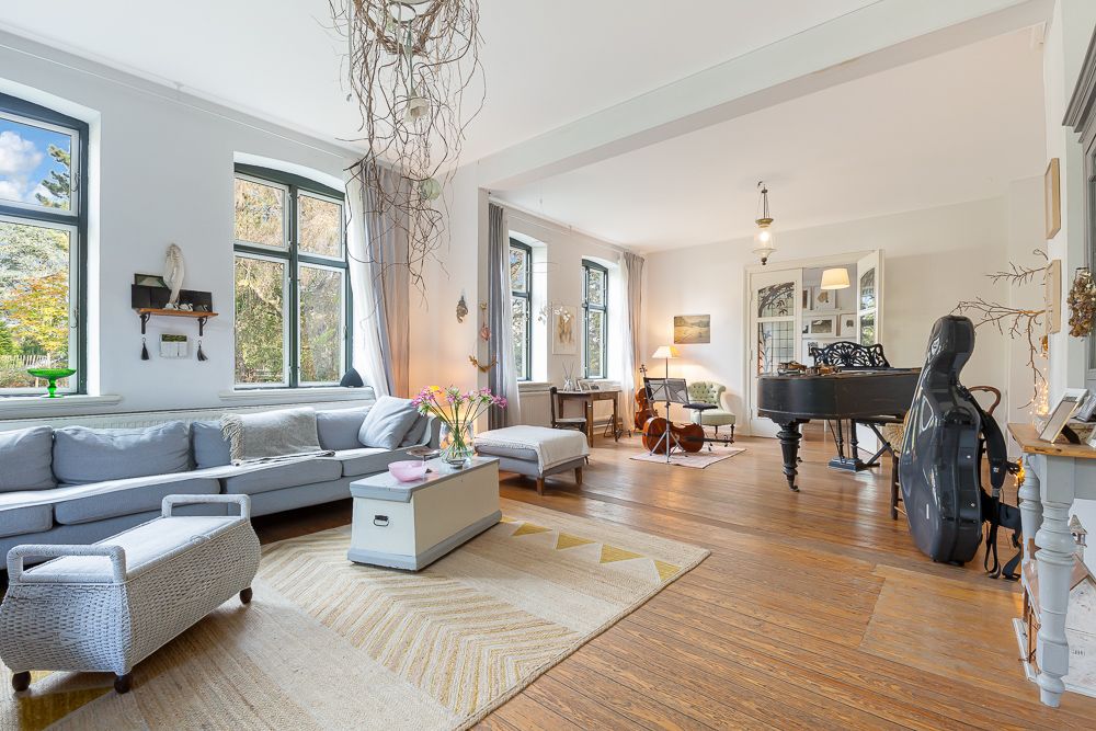 Helles Wohnzimmer mit Ecksofa, Couchtisch, Klavier und großen Fenstern.