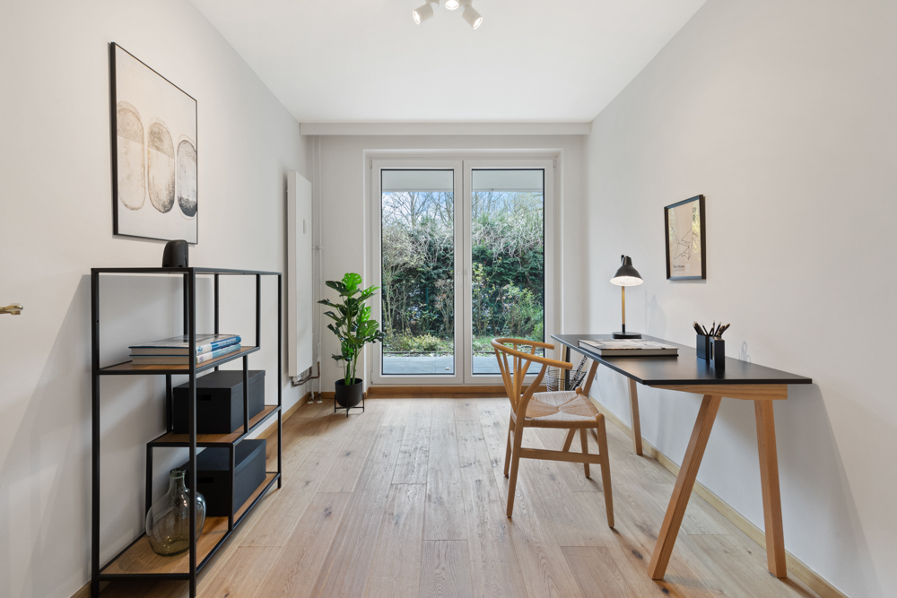 Helles Arbeitszimmer mit Schreibtisch, Stuhl, Regal und doppelflügeliger Glastür zum Garten.