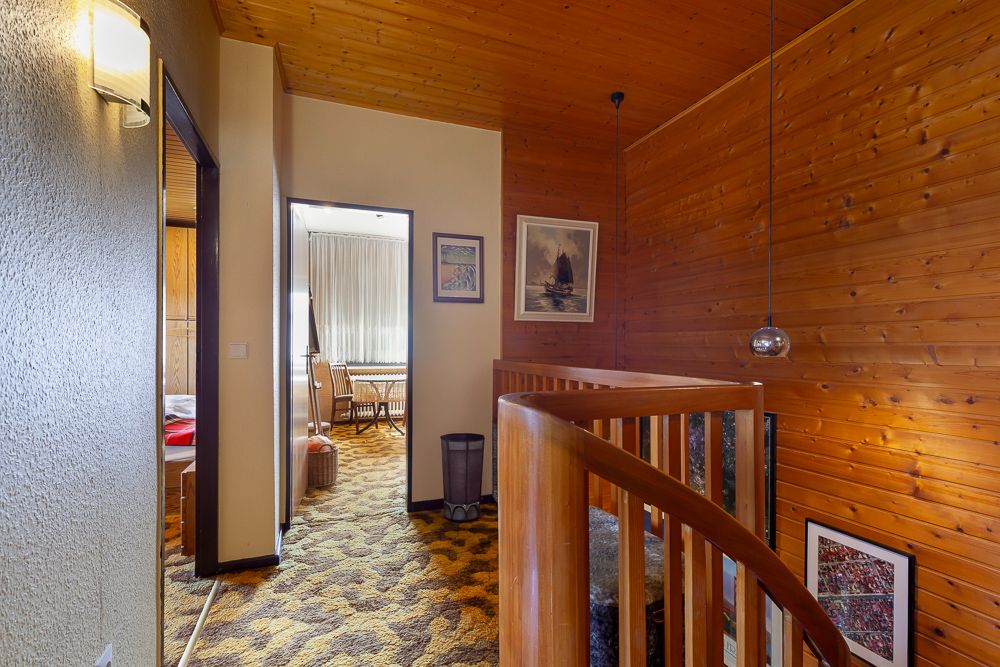 Flur mit Holzvertäfelung, Teppichboden und Zugang zu einem Zimmer mit großen Fenstern.