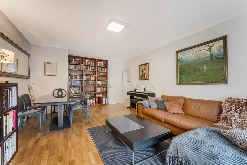 Wohnzimmer mit braunem Sofa, Couchtisch, Bücherregal, Esstisch und Klavier.