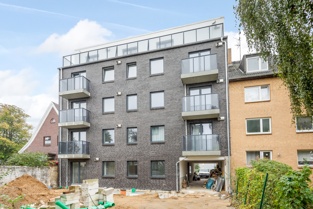 Modernes Wohngebäude mit Balkonen und dunkler Fassade, im Vordergrund eine Baustelle.