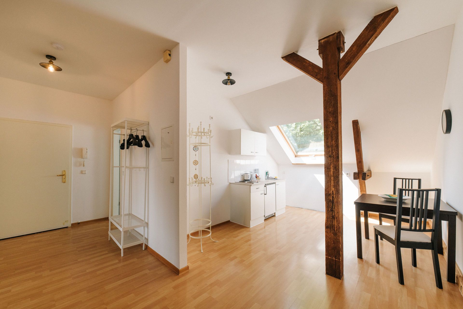 Helles Zimmer mit Holzboden, Küchenzeile, Esstisch, Stühlen und sichtbaren Holzbalken.