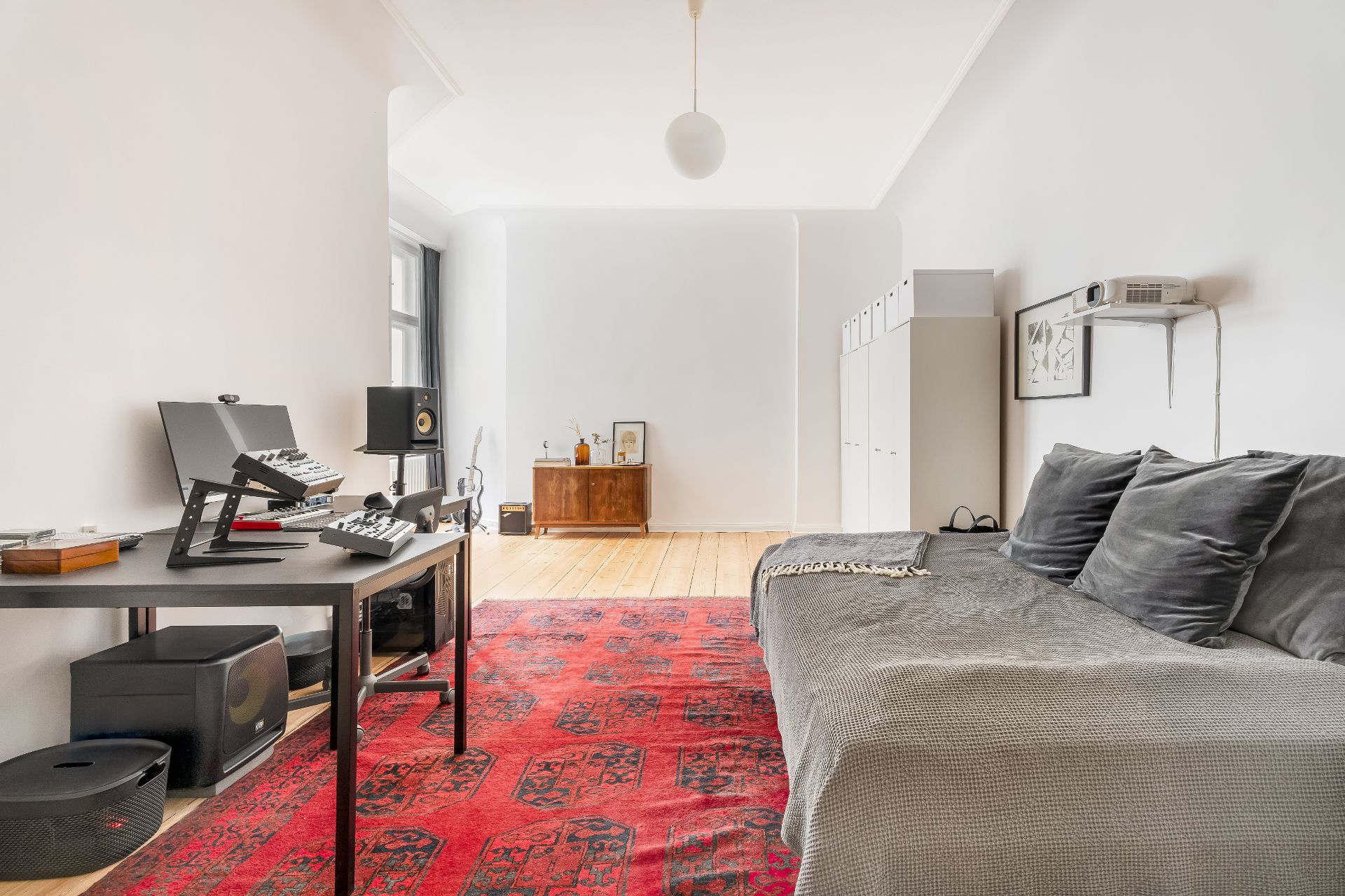 Helles Wohnzimmer mit rotem Teppich, Sofa, Schreibtisch und Schränken auf Holzfußboden.