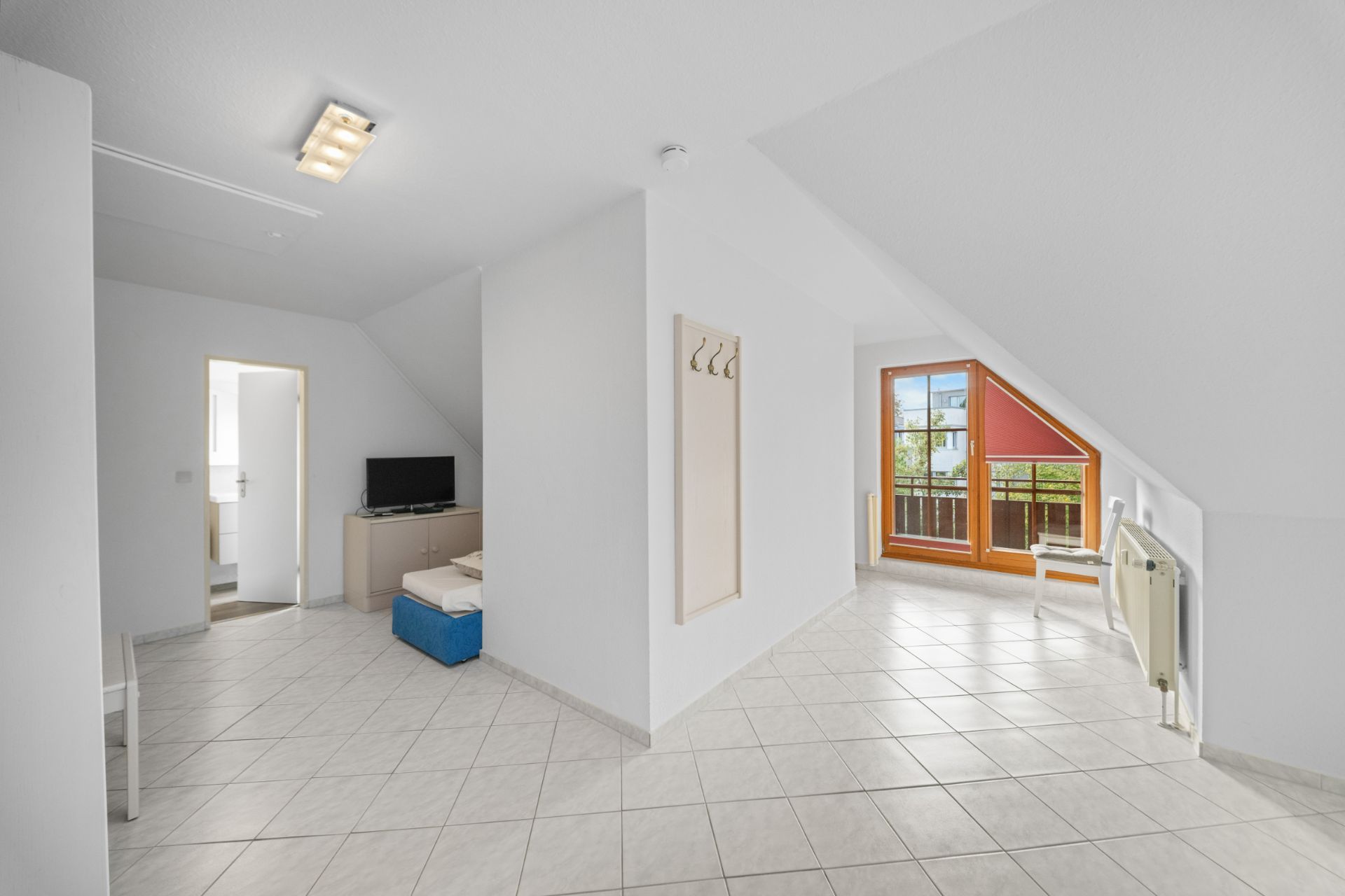 Helles Dachgeschoss mit Fliesenboden, Fenstertür zum Balkon und Wandgarderobe.