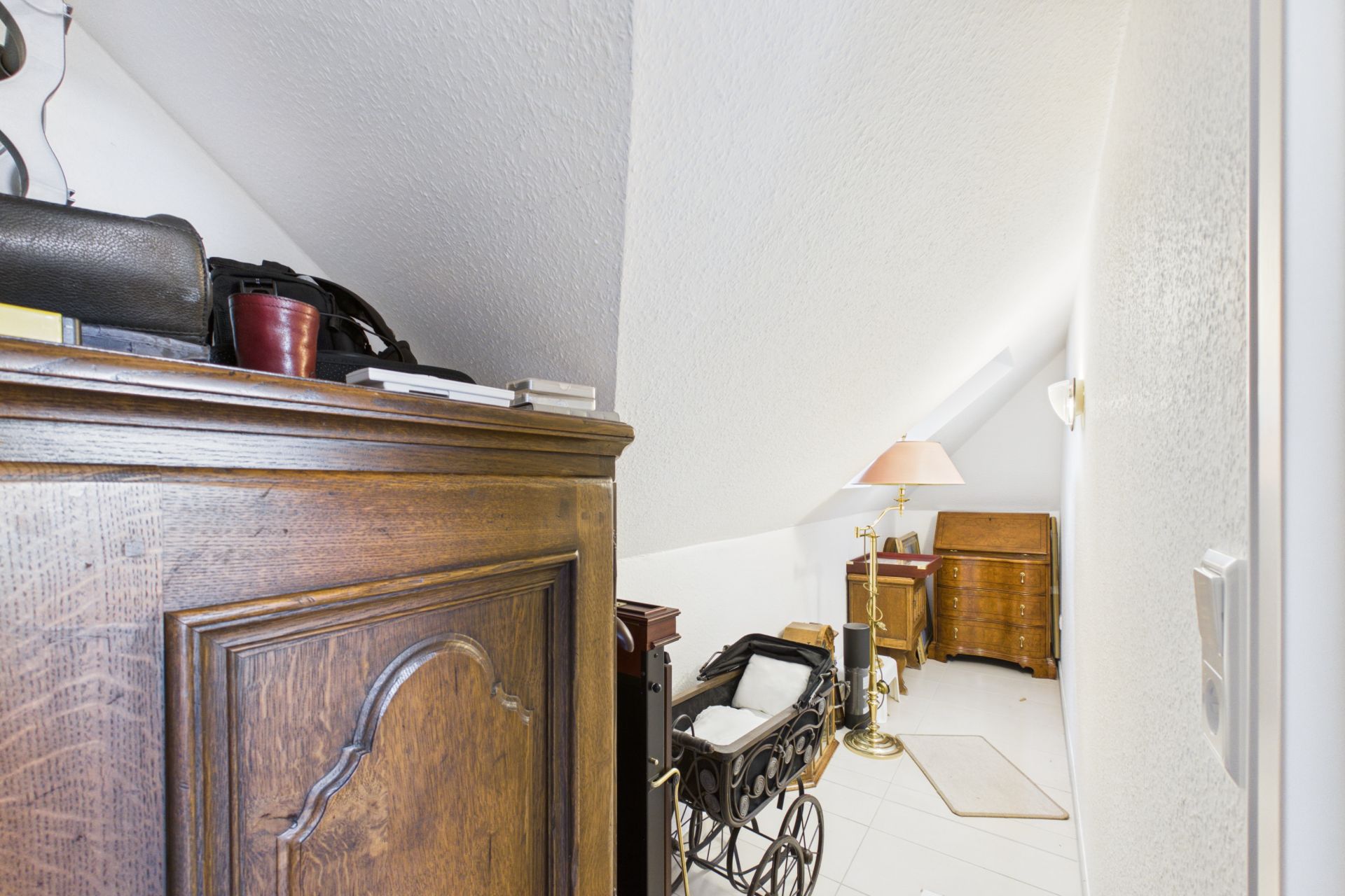 Dachzimmer mit Schräge, Altholzmöbeln, Stehlampe und Kinderwagen.