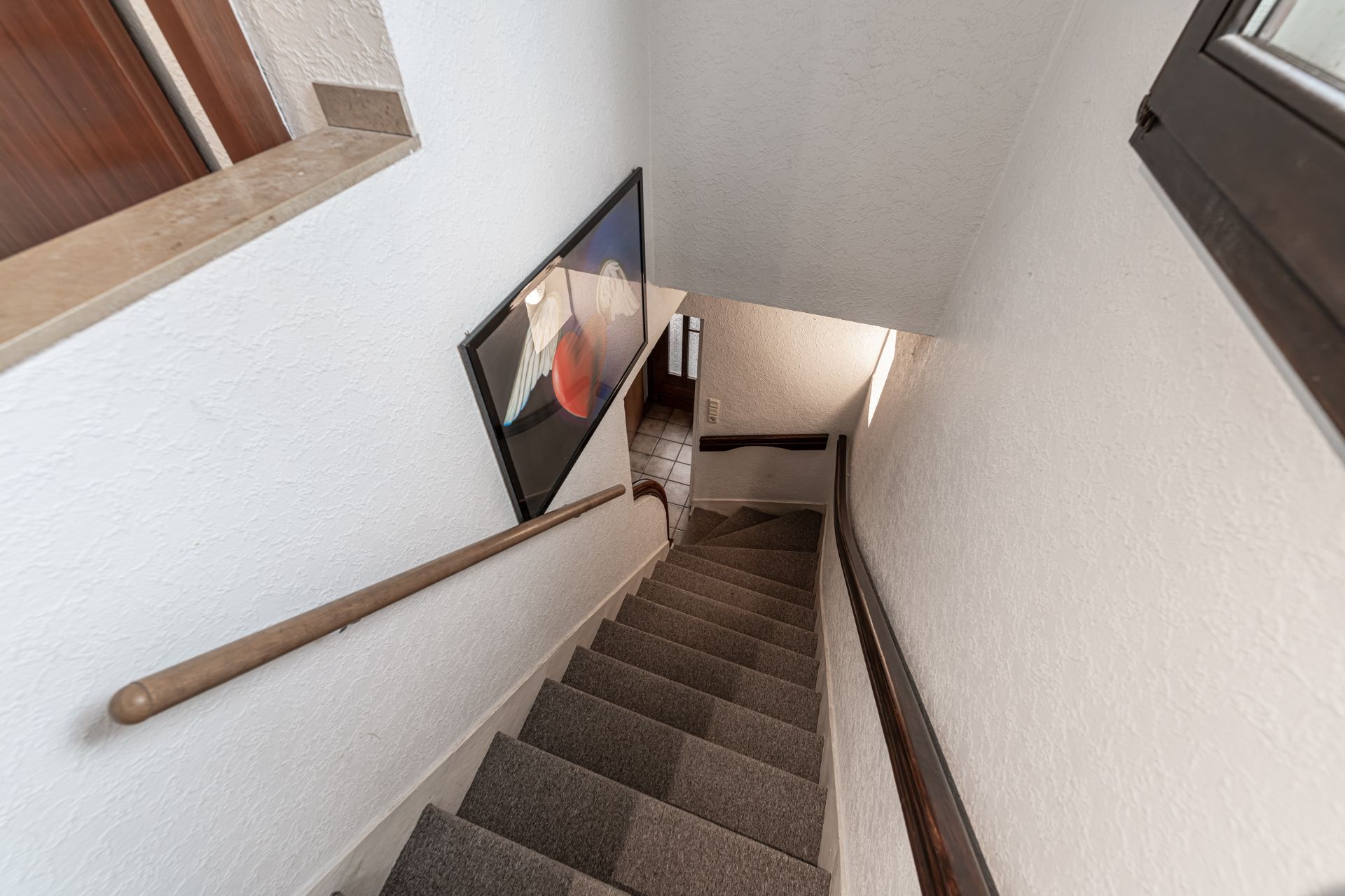 Teppichbedeckte Treppe mit Handlauf und Bild an der weißen Wand in einem Wohnhaus.