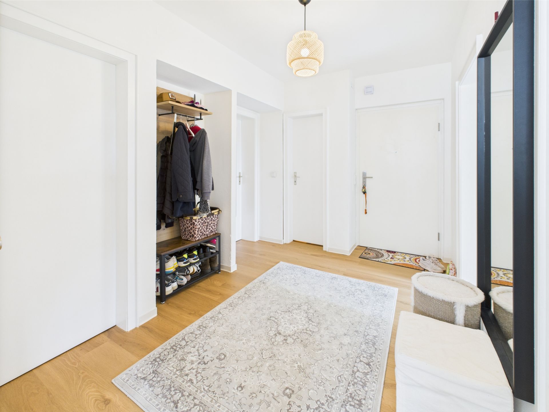 Heller Flur mit Teppich, Garderobe, Spiegel und mehreren Türen.