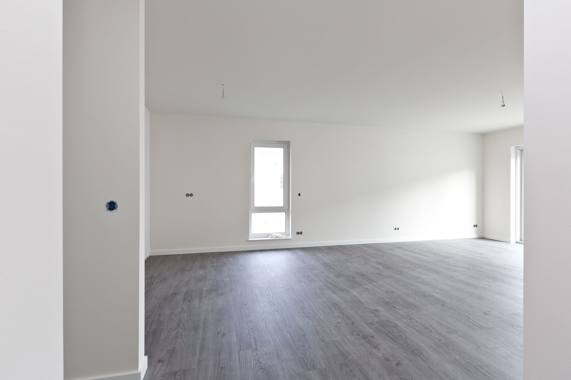Leerer Raum mit hellen Wänden und grauem Boden, Fenster an der Wand.
