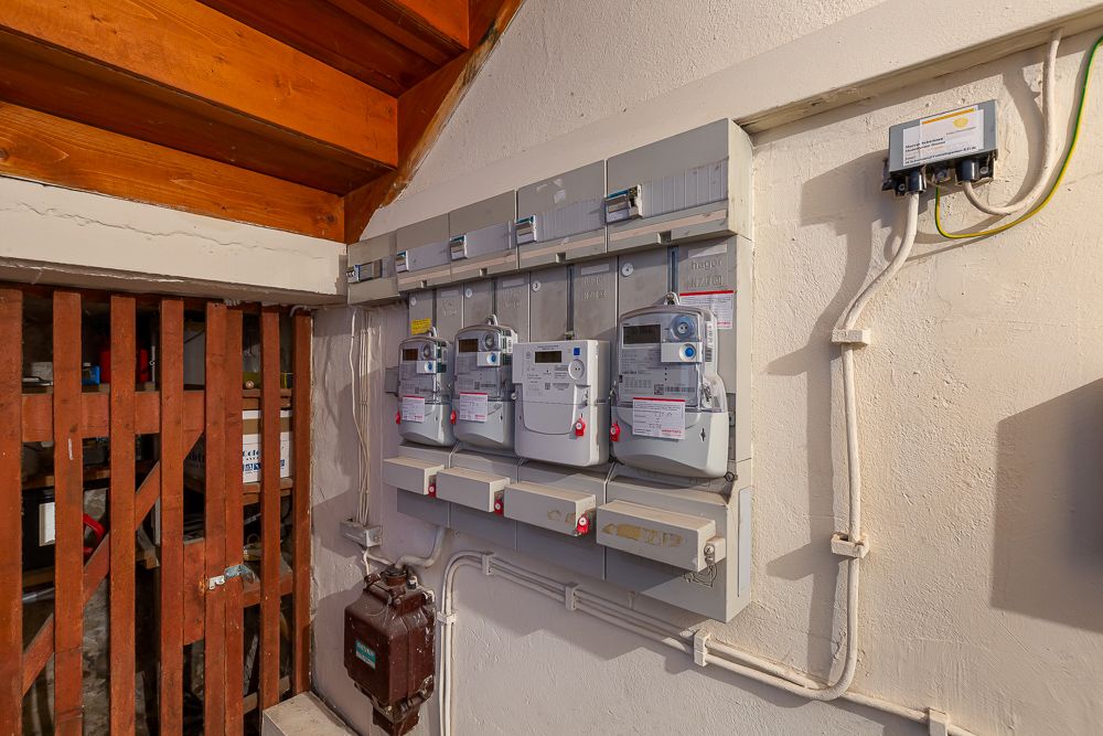 Mehrere Stromzähler und Sicherungskästen an einer Wand in einem Kellerraum.