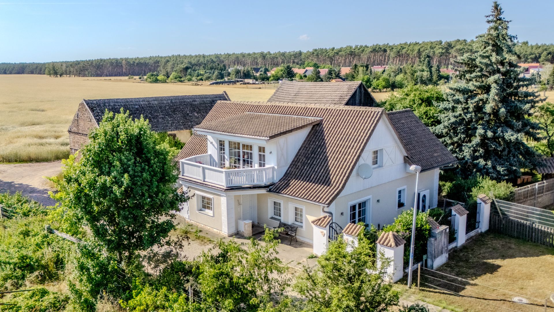 Weißes Einfamilienhaus mit Balkon und Garten, umgeben von Bäumen und Feldern.