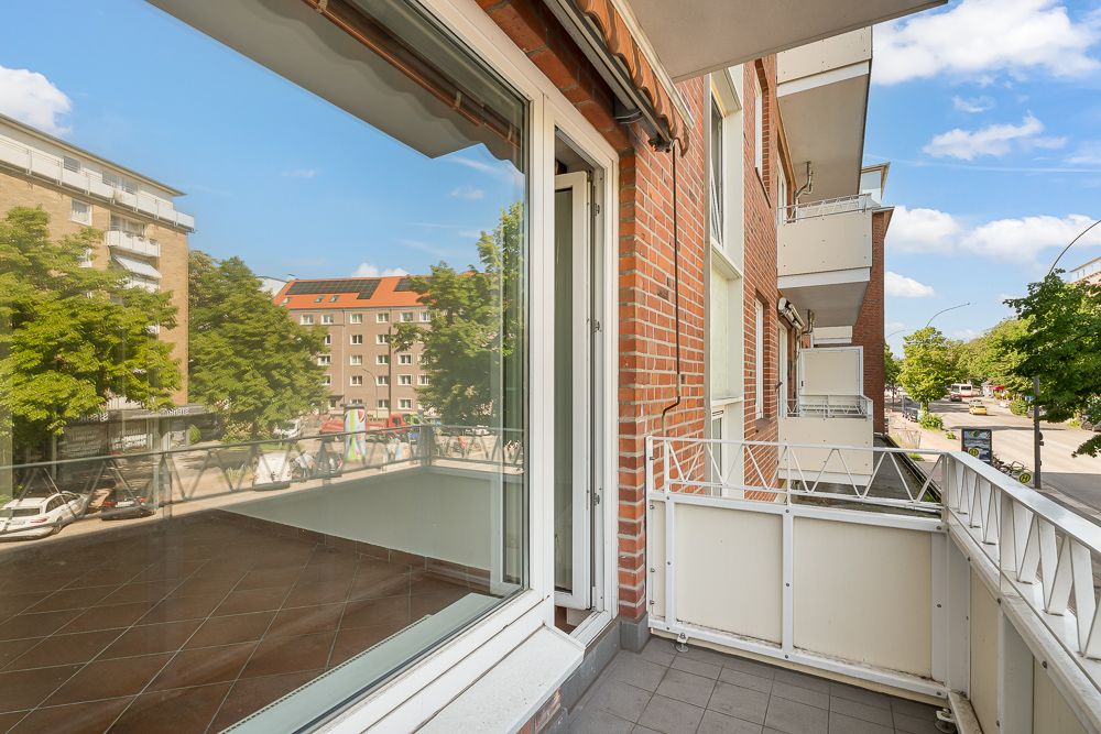 Balkon mit weißem Geländer an einem Wohnhaus, Blick auf Straße und Bäume.