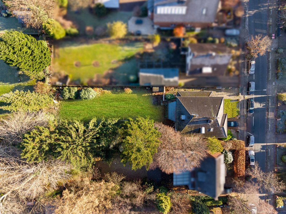 Luftaufnahme eines Wohnhauses mit großem Garten und Bäumen, daneben eine Straße mit geparkten Autos.