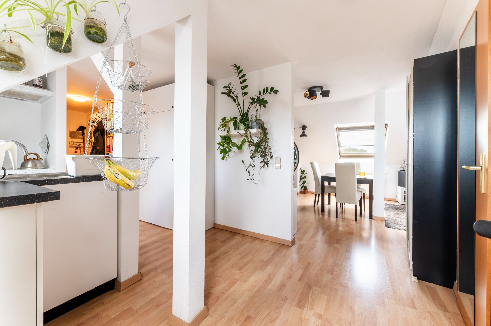 Helle Wohnung mit offenem Essbereich, Holzfußboden und vielen Pflanzen an den Wänden.