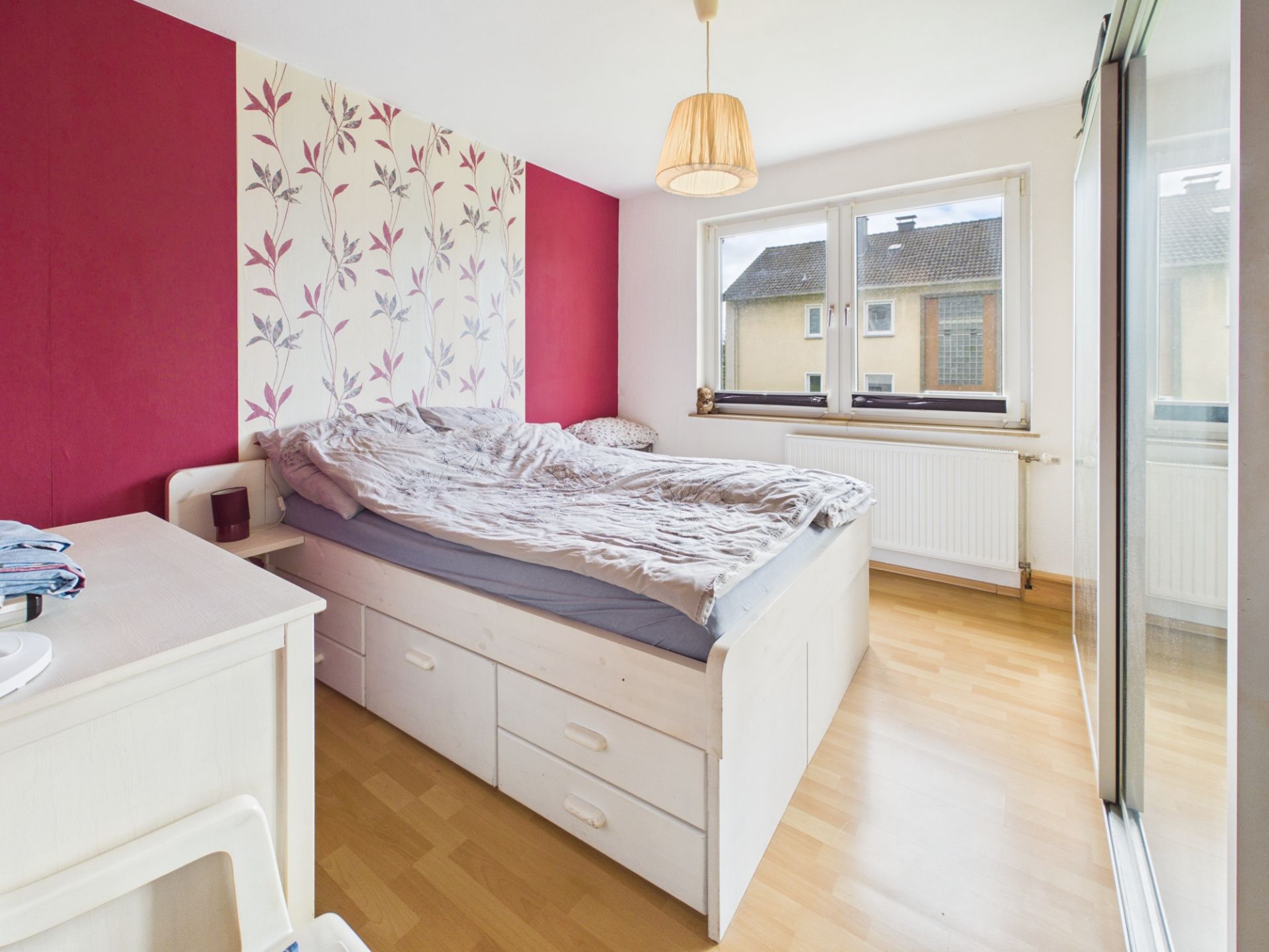 Helles Schlafzimmer mit Doppelbett, gemustertem Wandbereich und großem Fenster.