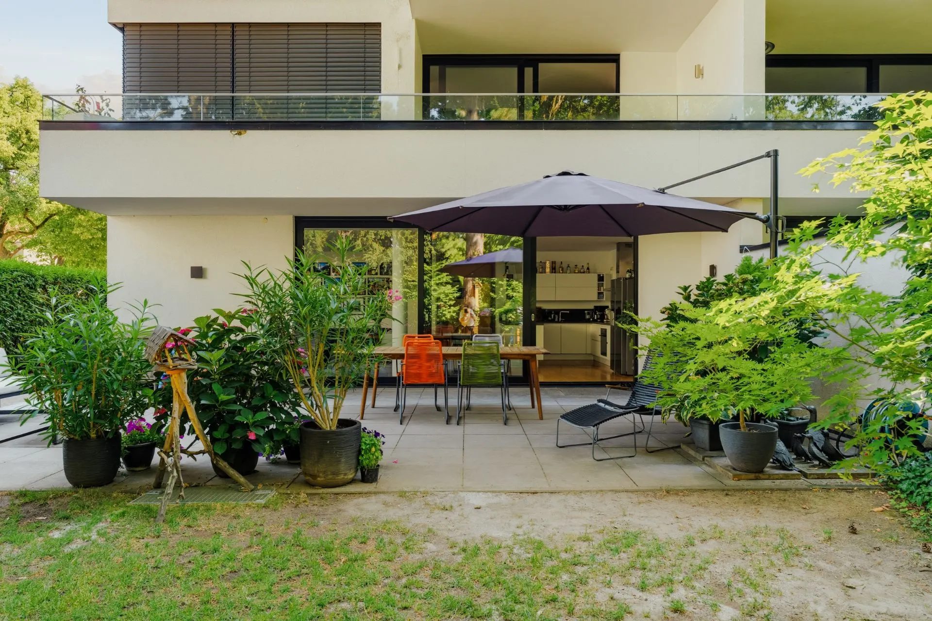 Moderne Terrasse mit Sitzbereich, großem Sonnenschirm und vielen Pflanzkübeln vor einem Wohnhaus.