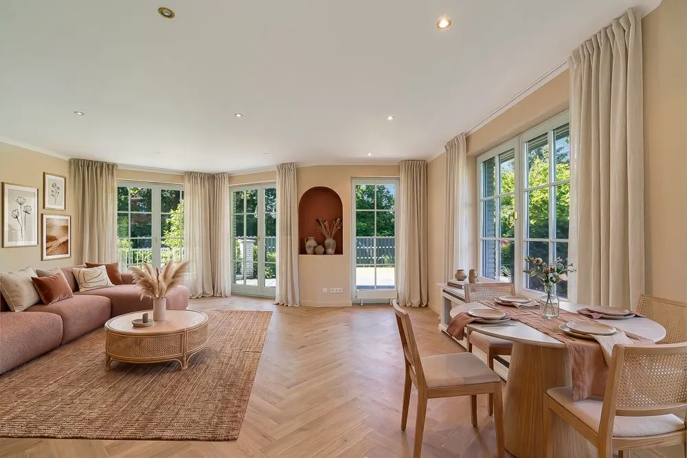 Helles Wohnzimmer mit Sofa, Couchtisch, Esstisch und großen Fenstern mit Blick ins Grüne.