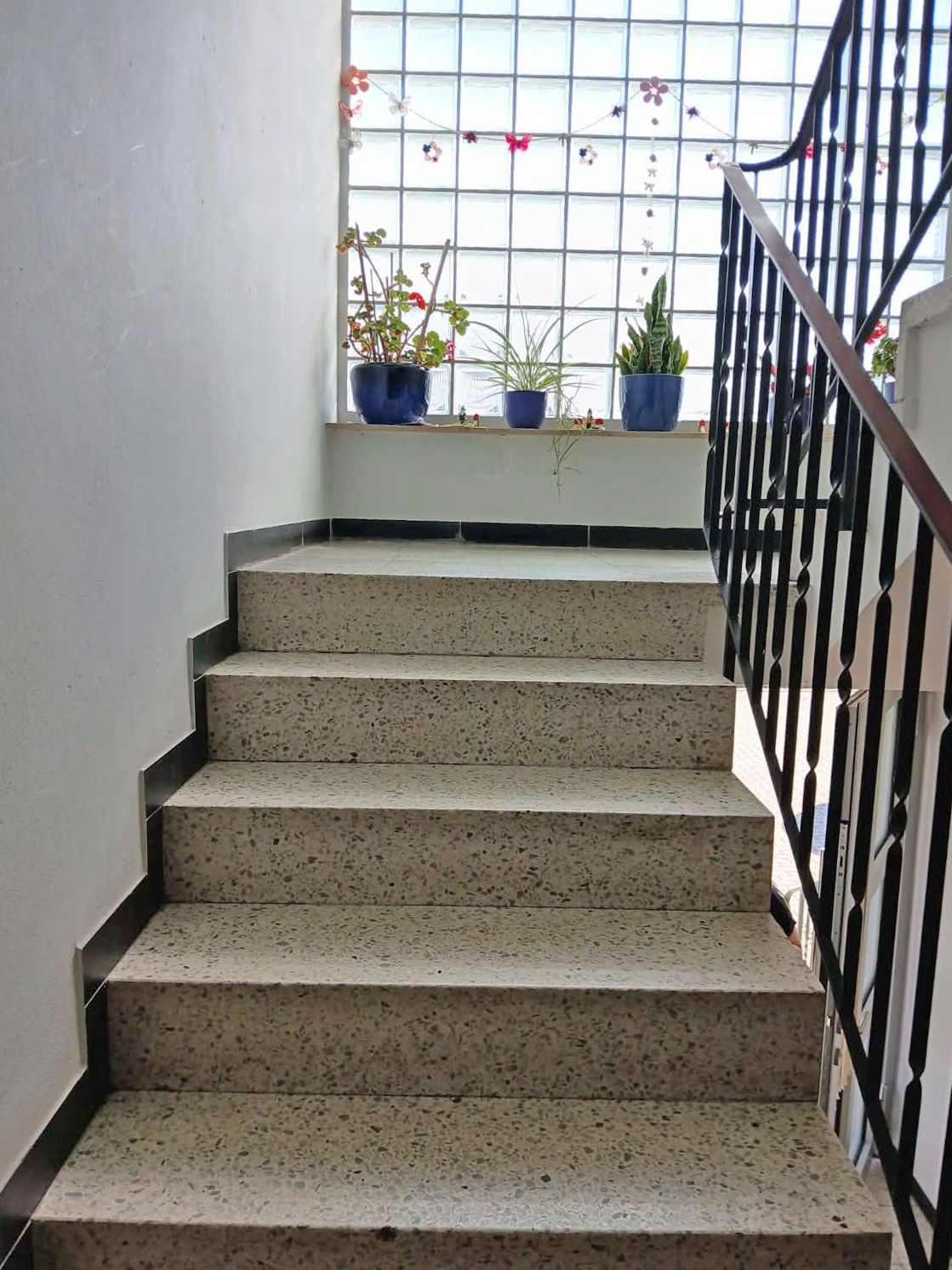 Treppe mit Geländer, oben Fenster mit Blumendekoration und Blumentöpfen auf der Fensterbank.