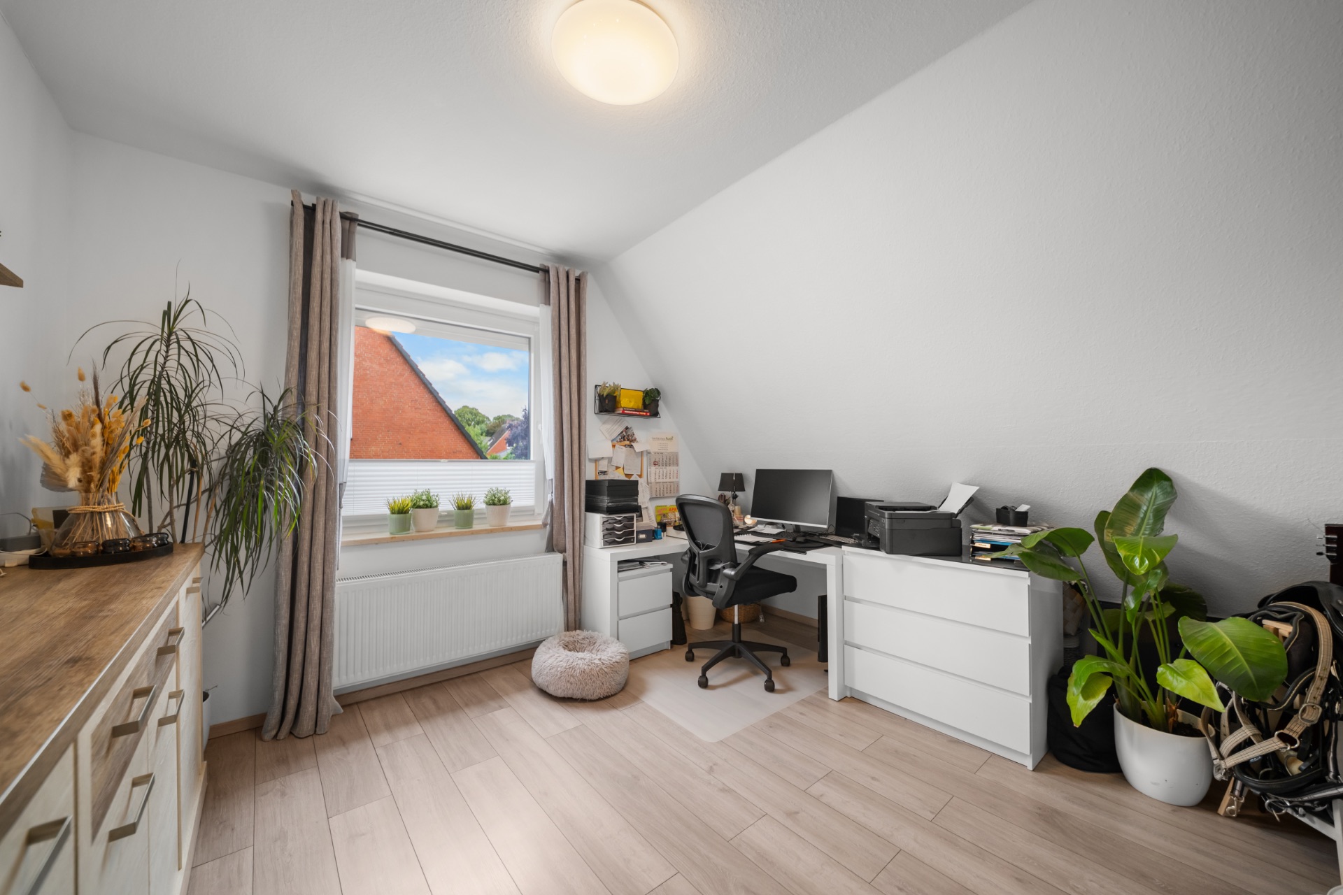 Helles Arbeitszimmer mit Schreibtisch, Stuhl, Pflanzen und großem Fenster mit Blick nach draußen.