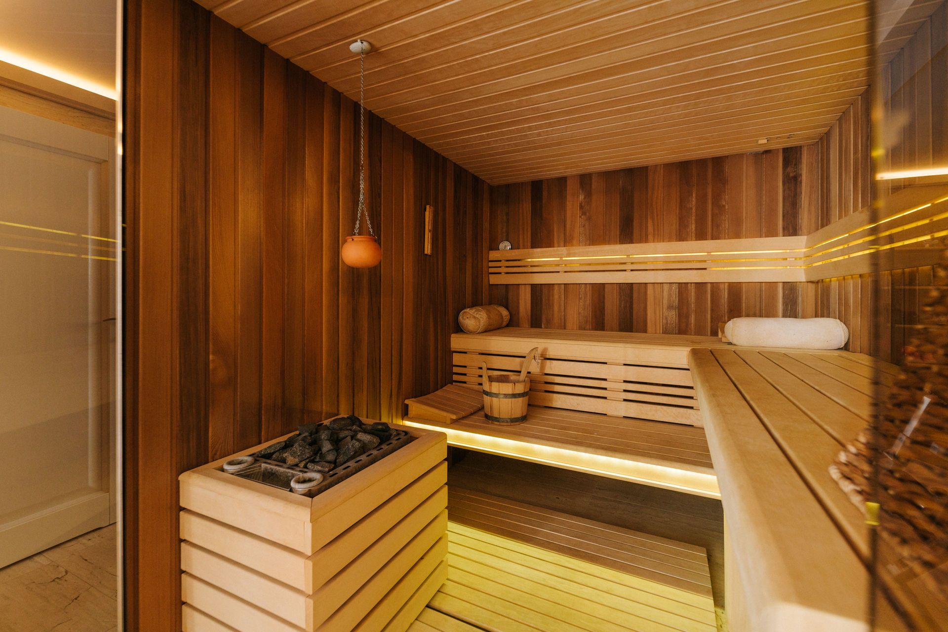 Moderne Sauna aus Holz mit Bänken, Steinen und Eimer.