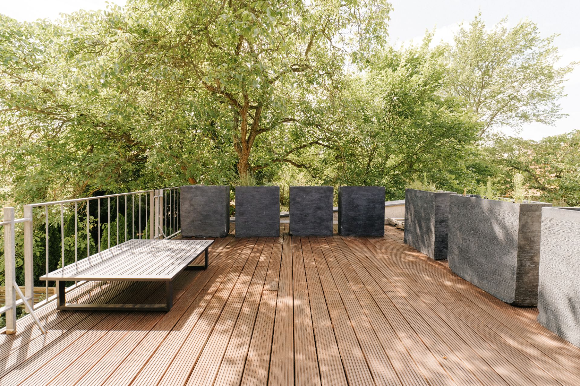 Große Holzterrasse mit Bank und Metallgeländer, umgeben von Bäumen.