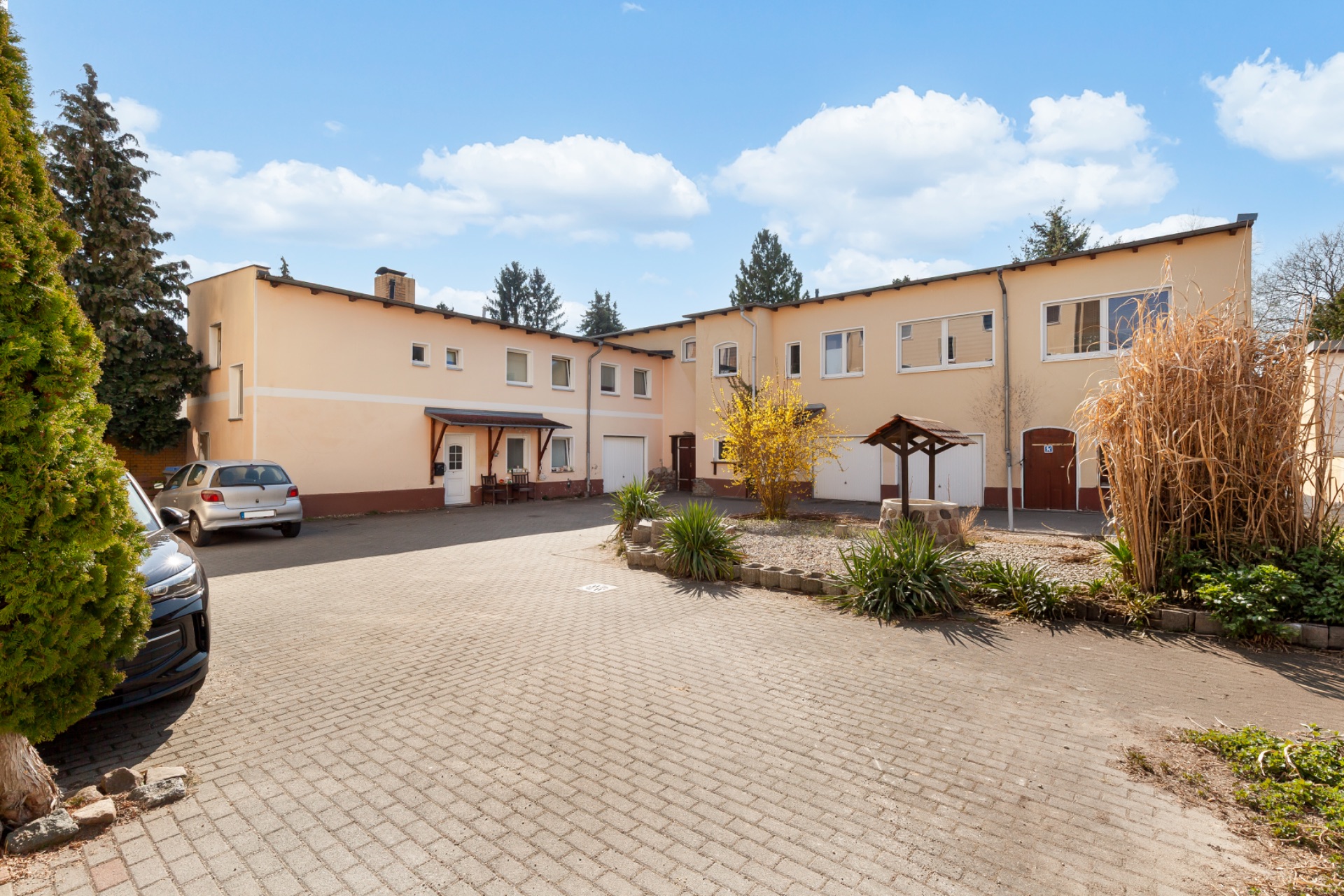 Gepflasterter Innenhof mit Wohngebäude, geparkten Autos und Gartenpflanzen.