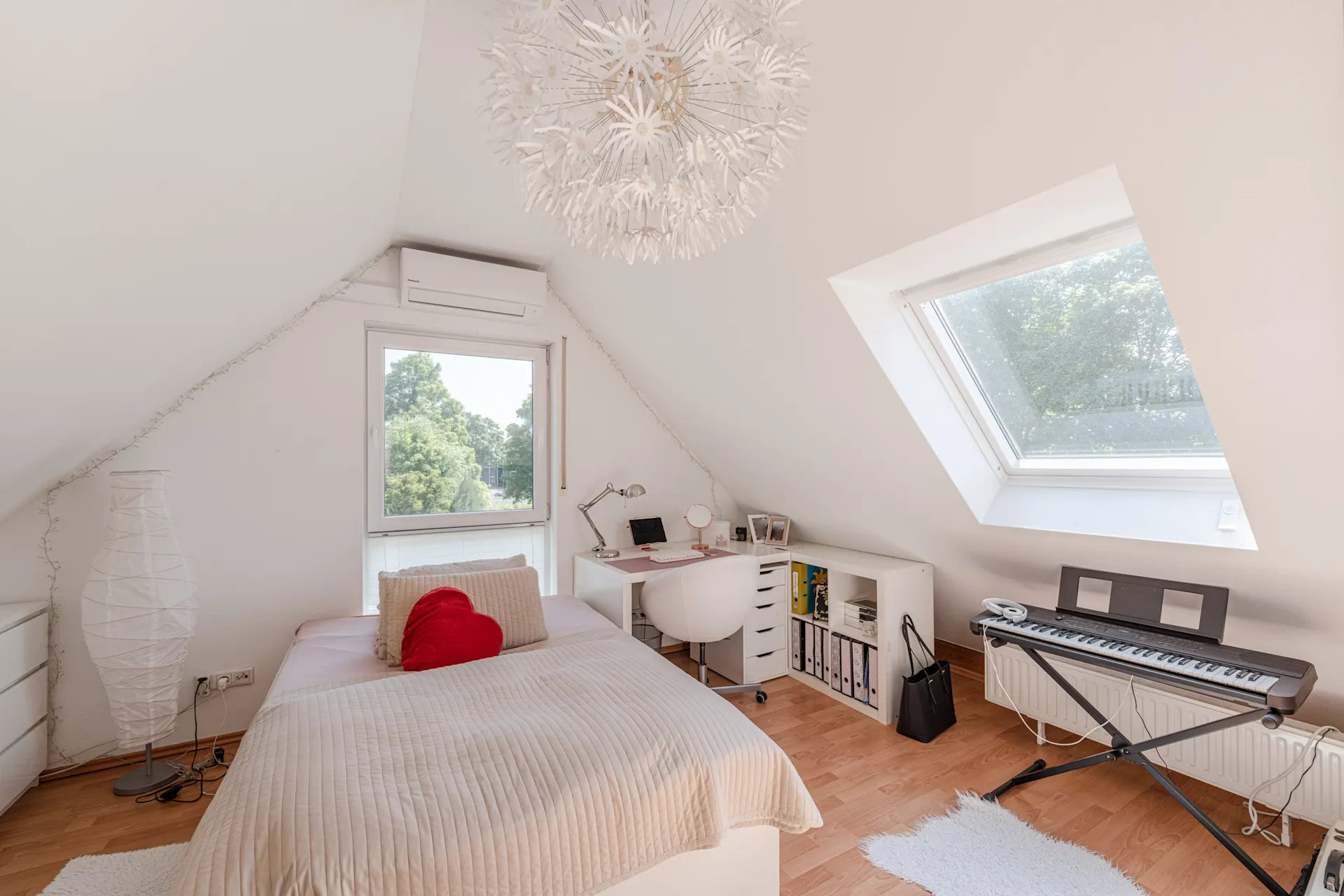 Helles Schlafzimmer mit Dachschräge, Bett, Schreibtisch, Fenster und E-Piano.