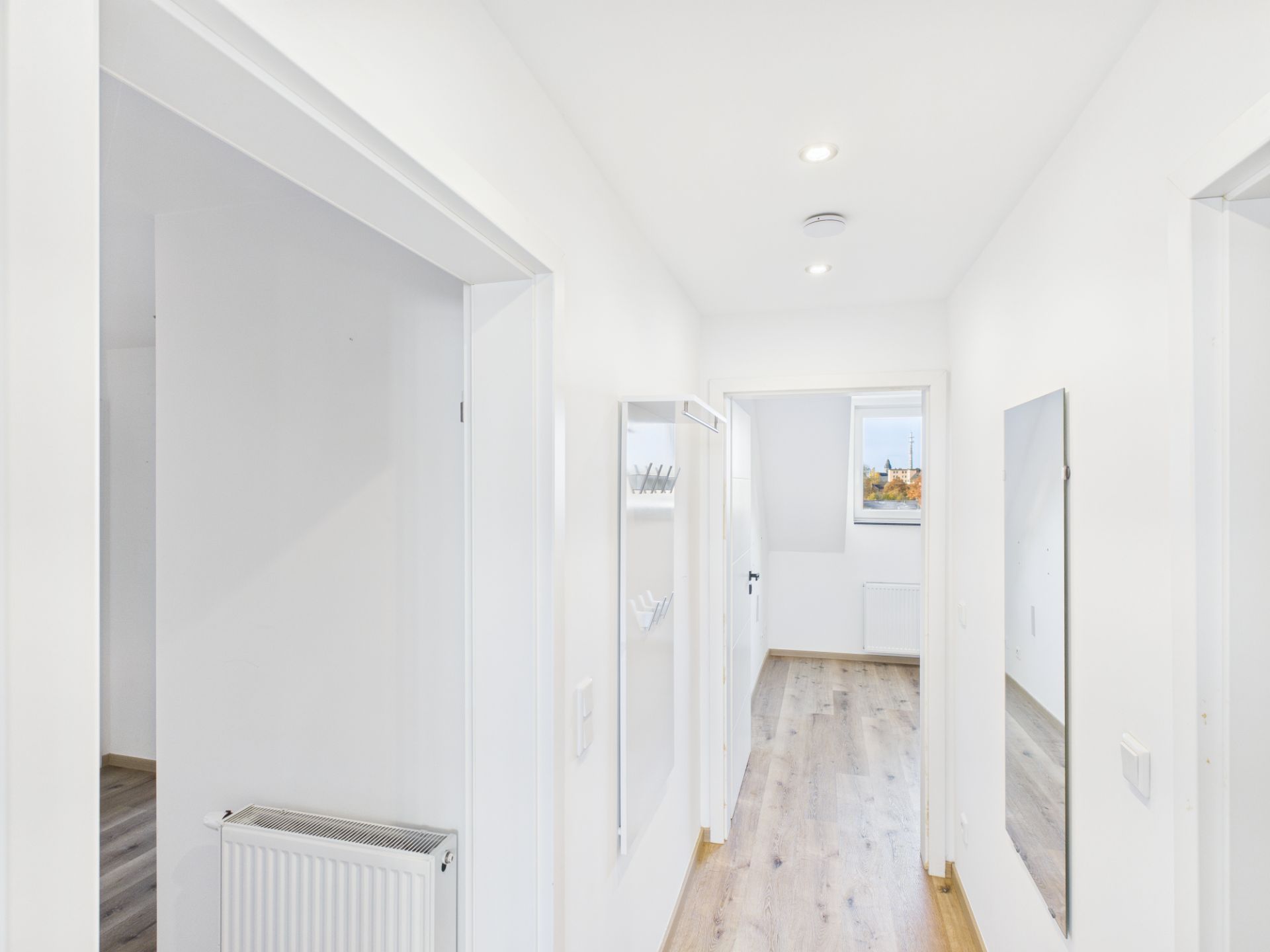 Heller Flur mit Holzboden, Spiegel und Garderobe, Türen führen in andere Räume.